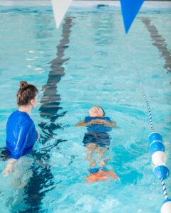 child floating on back during swim lessons supervised by woman