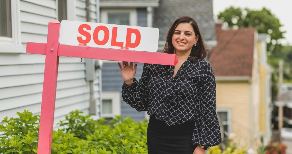 first time homeowner in front of house sold sign