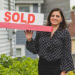 first time homeowner in front of house sold sign