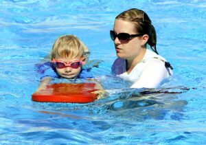 child practicing swimming with boogie board and assistance from woman